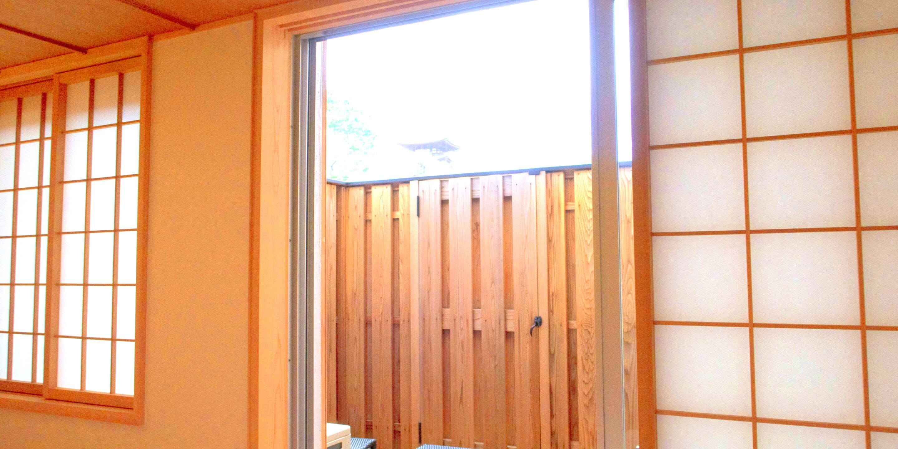Una habitación con puerta corredera de vidrio que da a una terraza de madera, una ventana con diseño de cuadrícula y una pared con motivo similar.