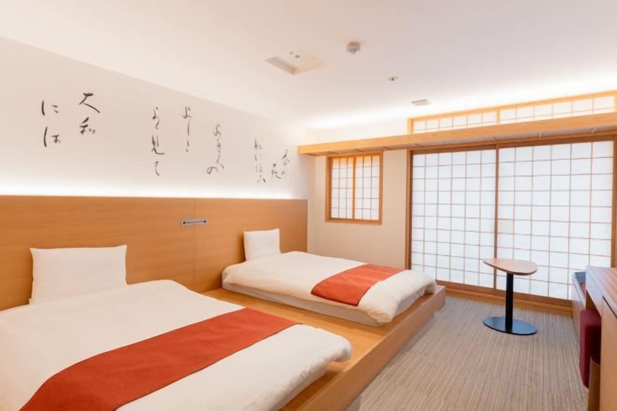 Habitación de hotel con dos camas, una mesita y vistas a una habitación tradicional japonesa.