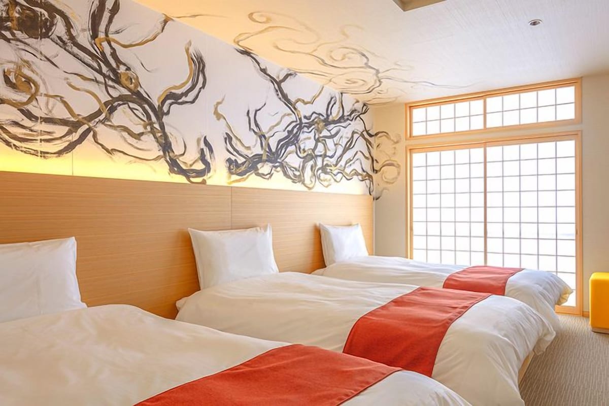 Habitación de hotel con dos camas, un ventanal grande y una obra de arte en la pared.