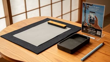 A wooden table with a black mat, a pen, a smartphone, and an audio guide stand.