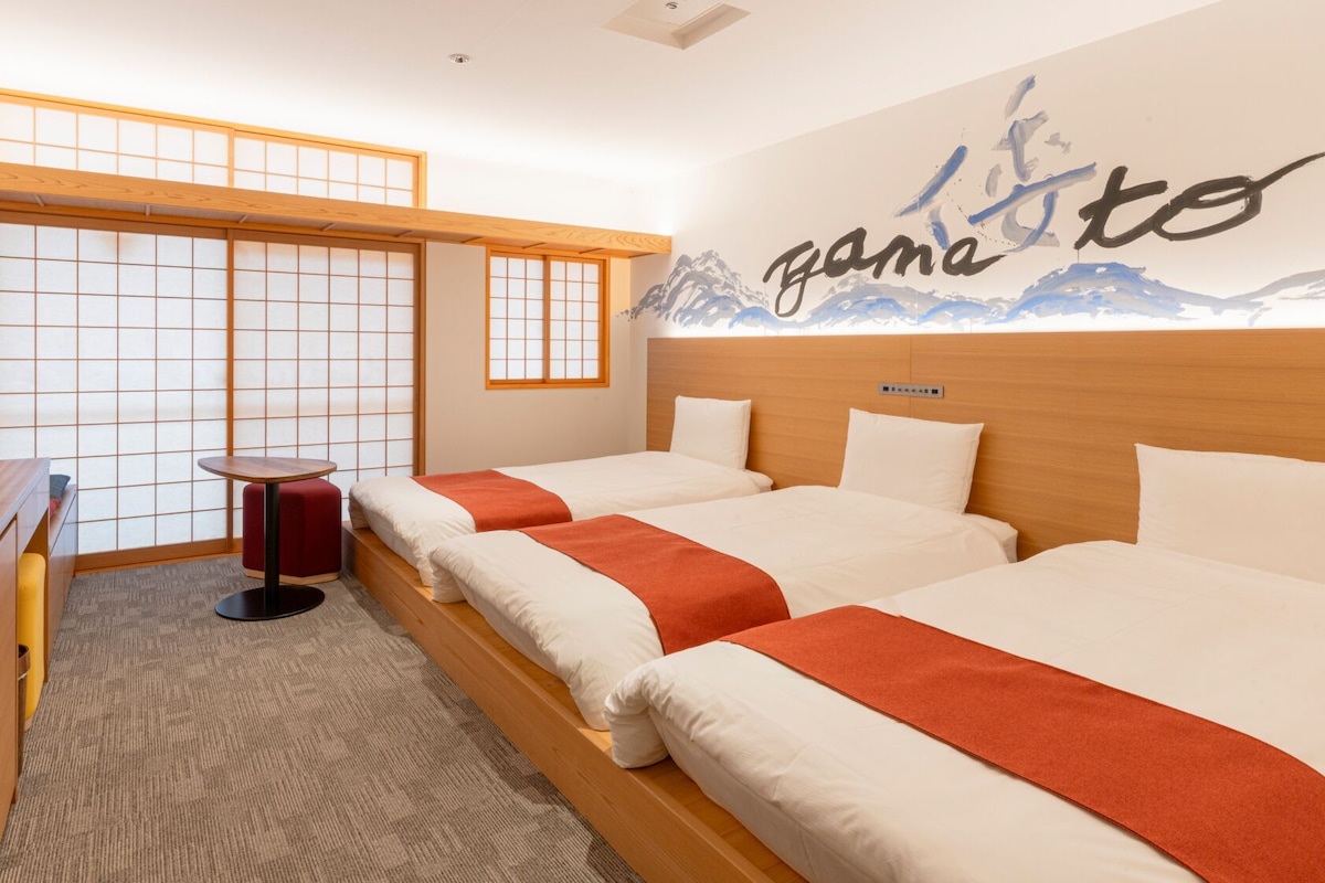 Habitación de hotel con dos camas, un escritorio, una mesita y un biombio japonés.