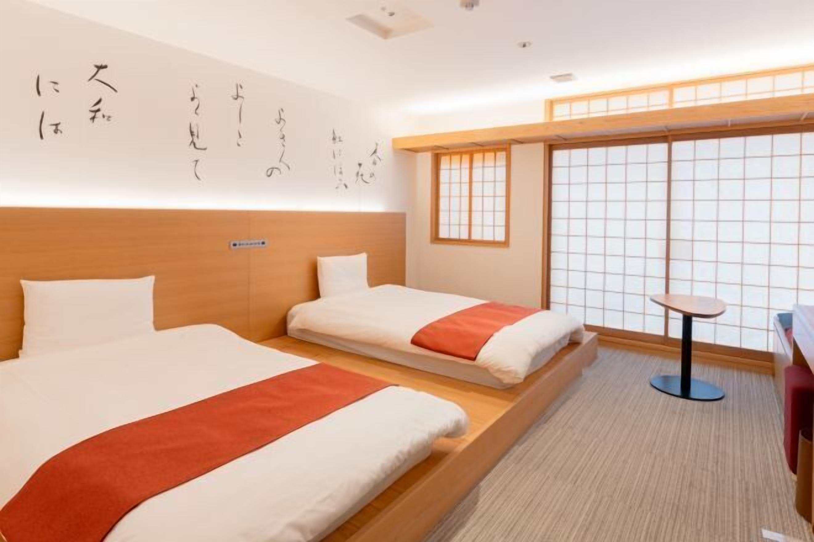 A hotel room with two beds, a small table, and a sliding shoji screen.