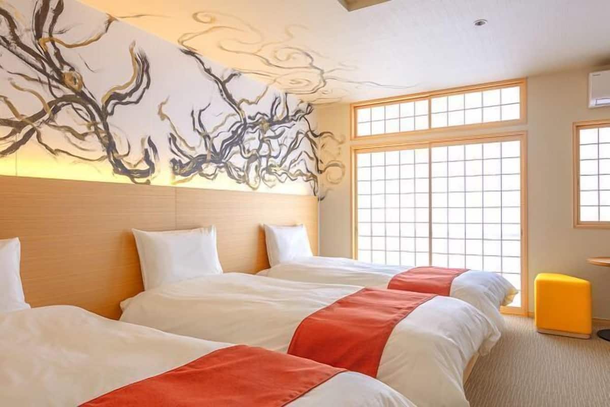 A hotel room with three beds, a large abstract wall art piece, and a view through a large window.