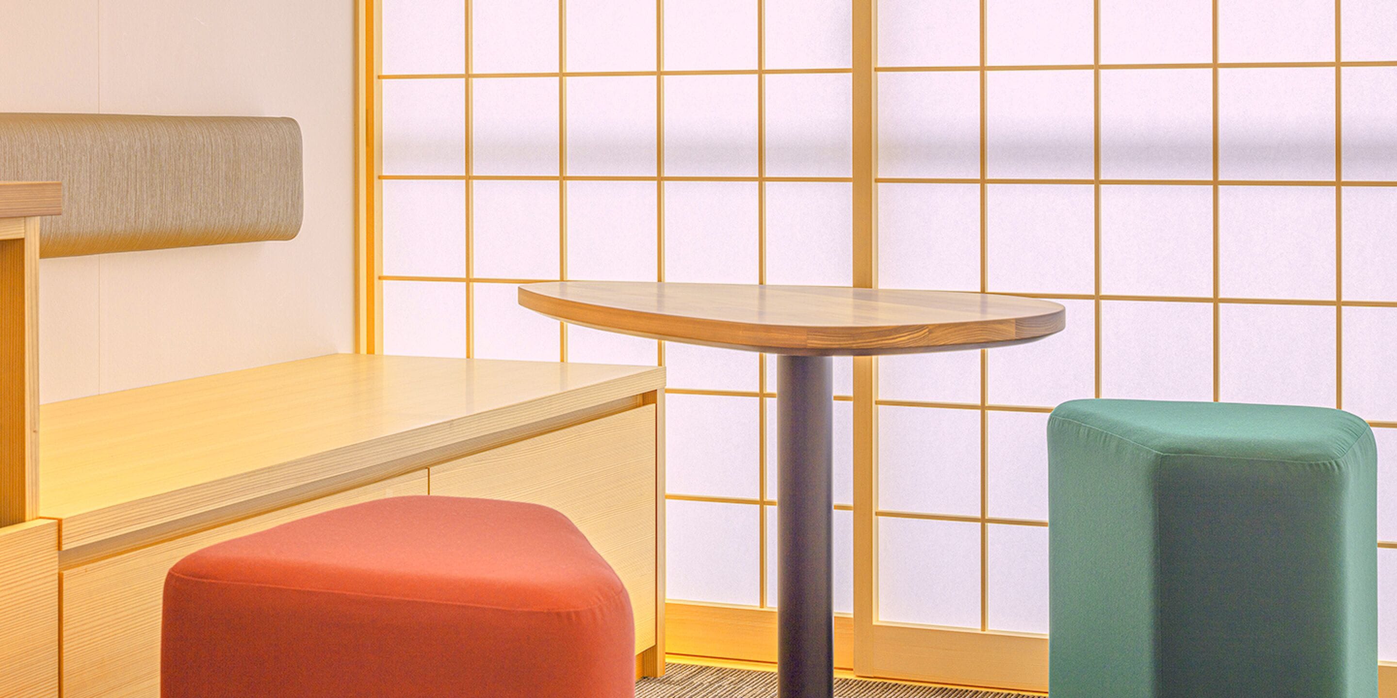 A room with a wooden table, a red stool, and a green stool.