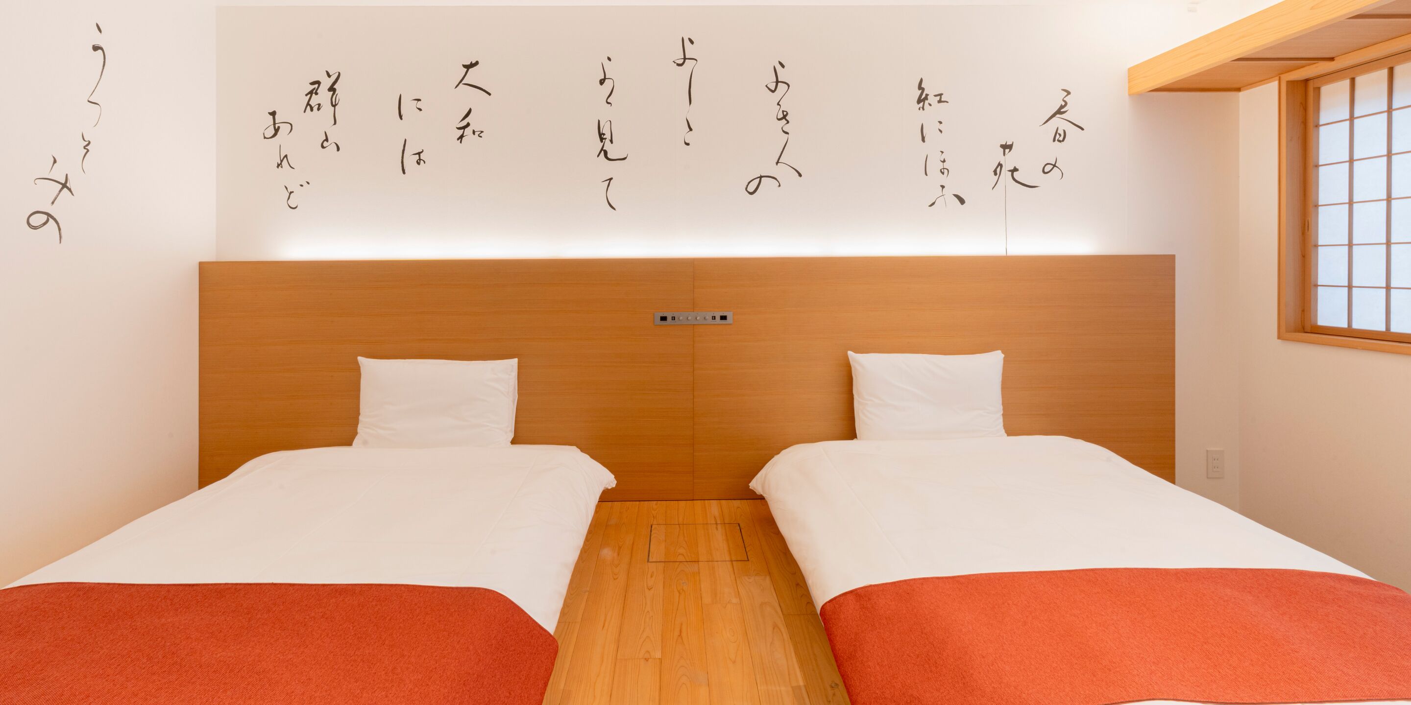 Quarto de hotel com duas camas, cabeceira de madeira, roupa de cama branca e caligrafia japonesa na parede.