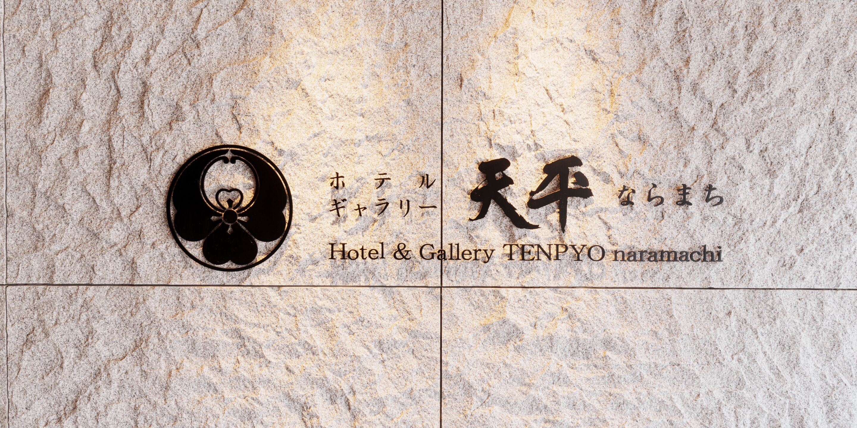 Un mur de pierre orné d’une inscription en japonais et du logo de l’hôtel-galerie TENPYO naramachi.