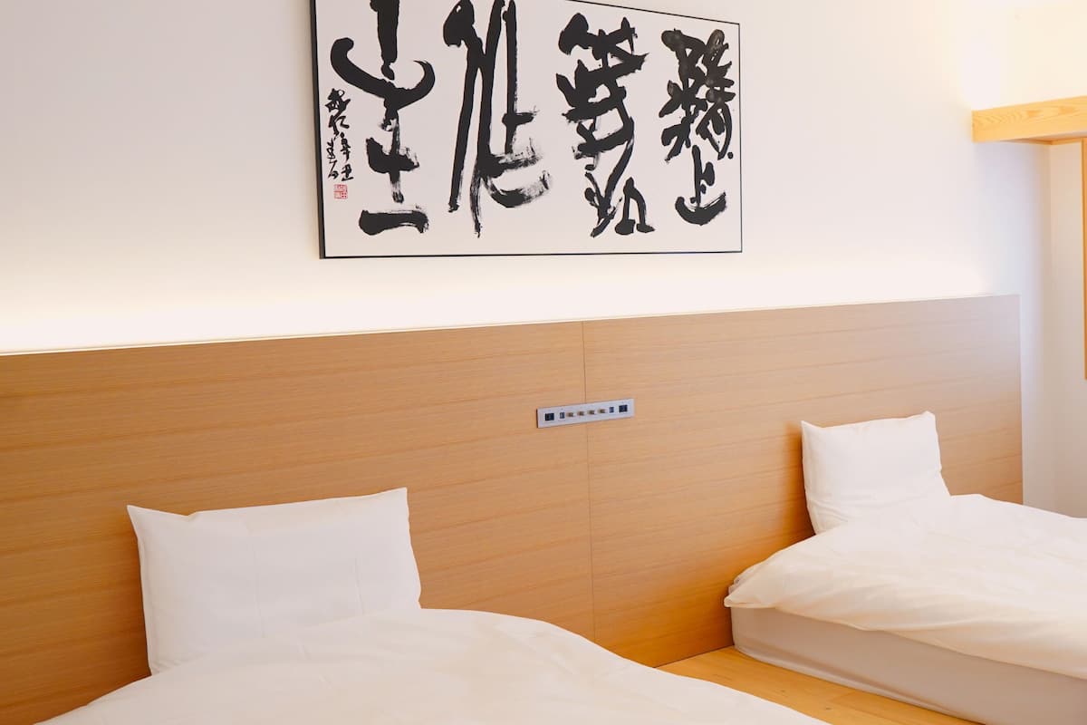 A hotel room with two beds, a wooden headboard, a window with a grid pattern, and a wall-mounted artwork with Chinese characters.