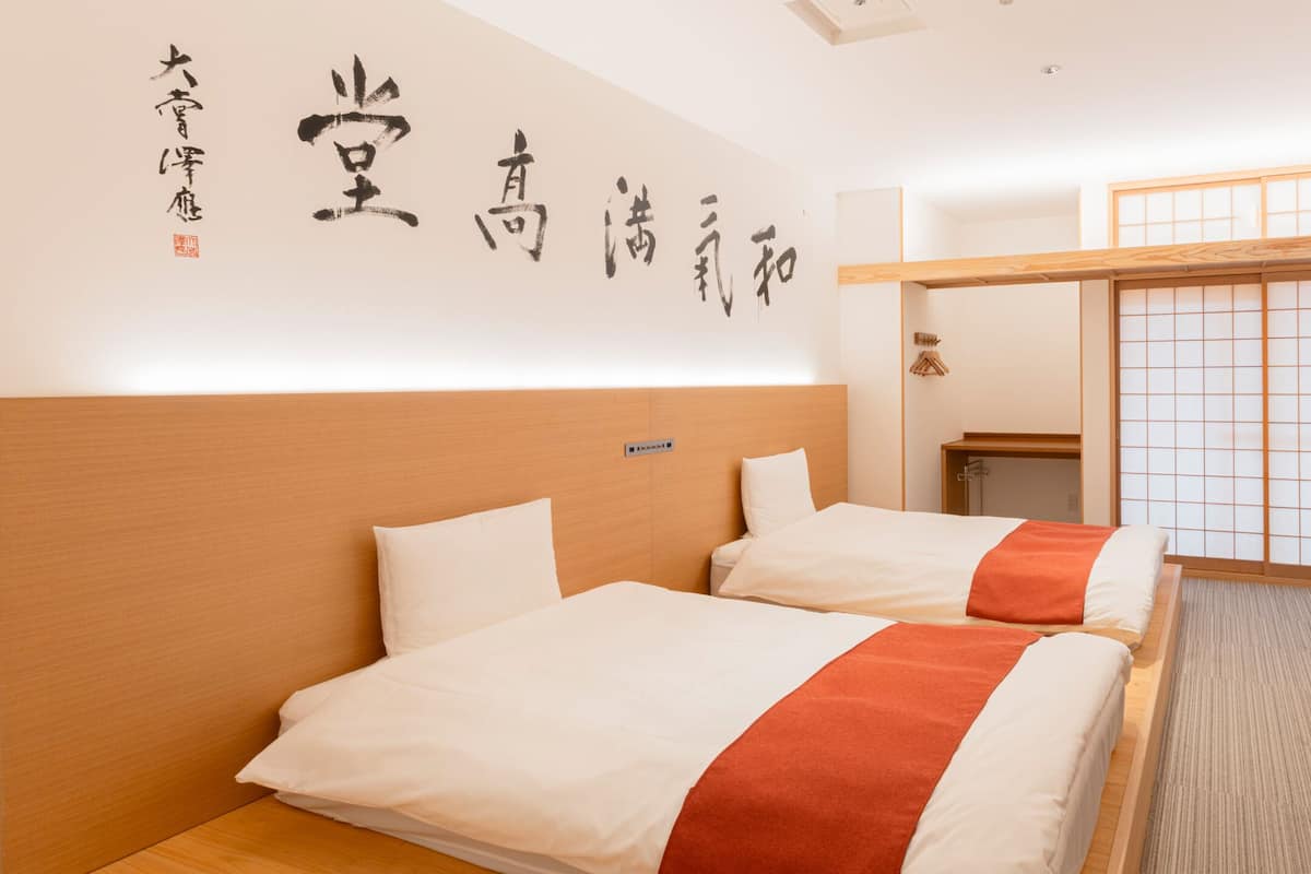 A hotel room with two beds, a desk, and a sliding shoji screen.