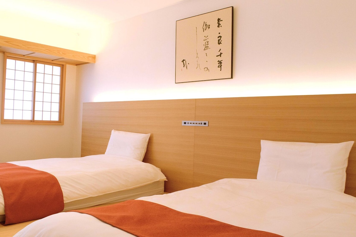 Habitación de hotel con dos camas, cabecera de madera, ventana con diseño de cuadrícula y un letrero colgado en la pared.