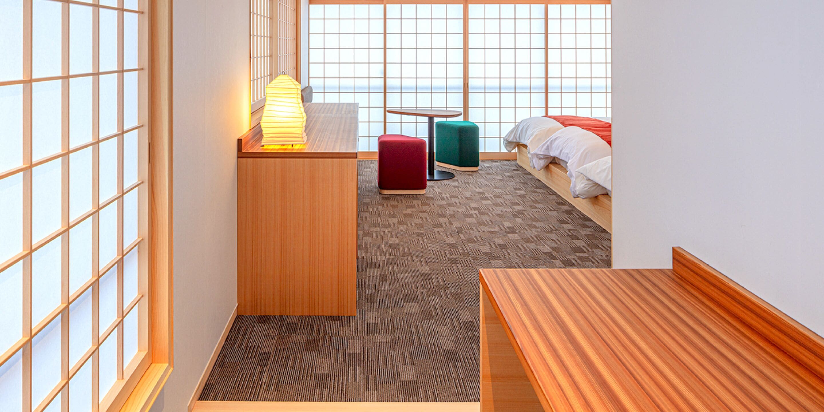 A compact hotel room with a bed, a small desk, a chair, a table, and a view of the sea through large windows.