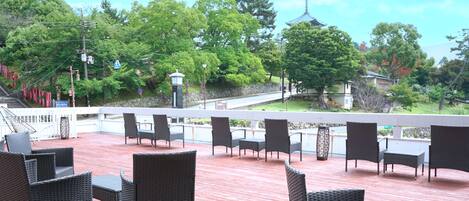 A covered outdoor seating area with wicker furniture and a view of a traditional pagoda and trees.