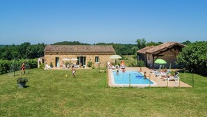 Una villa de piedra con piscina, mobiliario exterior y cancha de tenis.