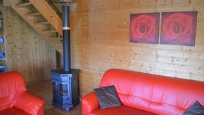 Una stanza accogliente con arredamento in legno, un divano in pelle rossa, un camino a legna nero e due quadri con rose sulle pareti.