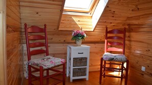 Una stanza piccola con pareti in legno e soffitto spiovente. Ci sono due poltrone rosse con cuscini floreali e un tavolino bianco con cesti in vimini. Un lucernario lascia entrare la luce naturale.