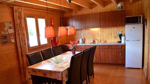 Una baita di legno con tavolo, sedie, angolo cottura e frigorifero.