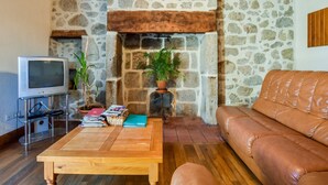 A cozy living room with a stone fireplace, a leather sofa, and a wooden coffee table. - Sénezergues Garden Hideaway (Sénezergues)