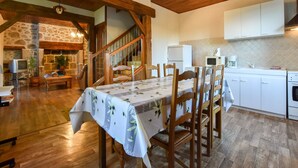 A cozy dining area with a wooden table and chairs, a stone wall, and a staircase leading to an upper level. - Sénezergues Garden Hideaway (Sénezergues)