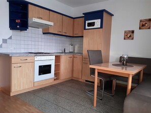 Una cucina compatta con mobili in legno, un forno a microonde integrato, un piano cottura e un'area pranzo con tavolo e sedia.