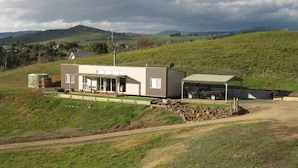 A modern house with a covered patio, a garage, and a stone wall. - Omeo Mountain Views. Peace and Tranquillity (Omeo)