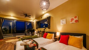 Ein Hotelzimmer mit zwei Betten, einem Deckenventilator, einem Balkon mit Tisch und Stühlen sowie Bildern an den Wänden.