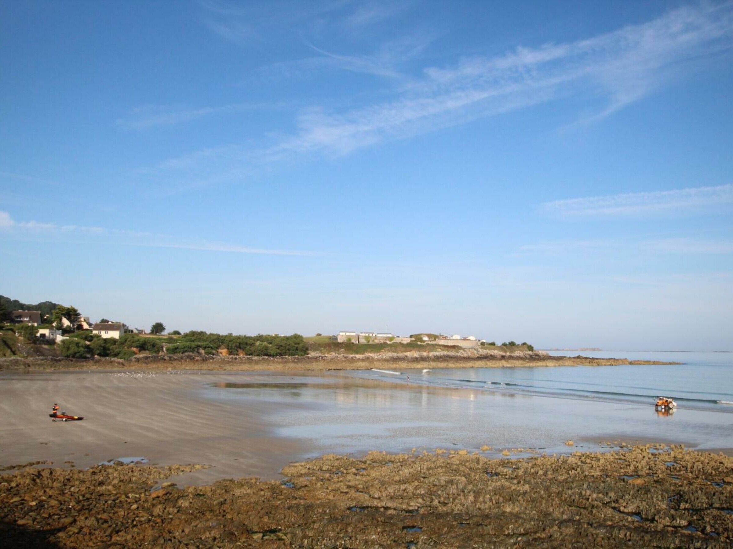 A coastal beach with rocky shorelines and buildings in the background.