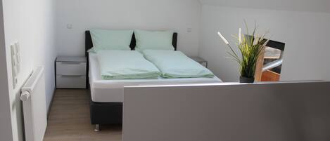 Un dormitorio con cama, mesita de noche, radiador y tragaluz.