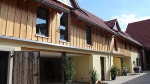 A wooden building with multiple windows and doors, a paved courtyard, and potted plants.