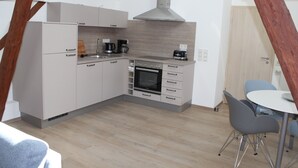 A compact kitchen with modern appliances, a dining area with a table and chairs, and a wooden ceiling structure.