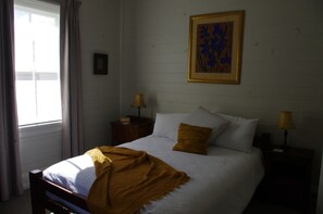 A bedroom with a bed, two bedside tables with lamps, a window with curtains, and a framed artwork on the wall. - Luxury Heritage Cottage In The Heart Of Town (Mittagong)