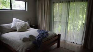 Quarto com uma cama grande, janela e vista para o verde lá fora.