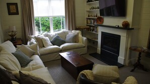 Uma sala de estar com sofá, mesa de centro, lareira e estante com objetos decorativos.