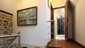 A staircase with stone walls and a wooden handrail, leading to a room with a glass door and a painting of birds. - Charming stone house in Villedieu with garden (Villedieu-les-Poêles)
