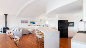 A modern kitchen with a black refrigerator, oven, and stove, a white island with bar stools, and a large window overlooking the living area. - Huey's Lookout - beachfront spacious pet friendly home (Blueys Beach)