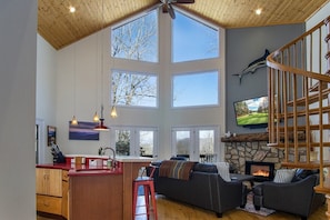 A spacious living area with a high ceiling, large windows, a fireplace, and a stone accent wall.