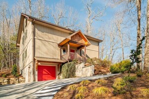 A two-story building with a red garage door, a balcony, and a stone retaining wall.