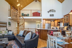 A spacious living area with a dark leather sofa, a wooden staircase, and a kitchen with wooden cabinets and a stainless steel refrigerator.
