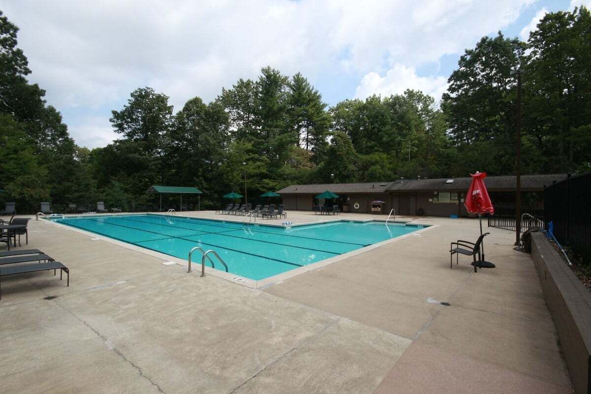 Une piscine rectangulaire entourée d’une terrasse en béton, avec des chaises longues et des parasols.