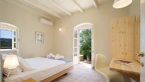 A bedroom with a bed, bedside table, lamp, and a view of the outdoors.