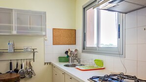 Une cuisine avec des armoires blanches, une cuisinière à gaz, une fenêtre et divers ustensiles de cuisine.
