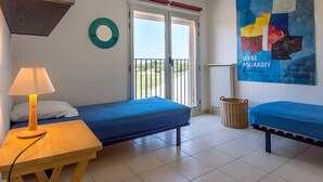 Une chambre avec deux lits, une table avec une lampe, une fenêtre donnant sur un beau paysage et un tableau accroché au mur.