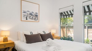 A neatly made bed with white and dark brown pillows, two bedside lamps, and a framed picture on the wall.