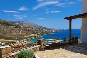 A terrace with a table and chairs overlooking a coastal landscape with a mountain in the distance. - Monolithos Villas (Andros)