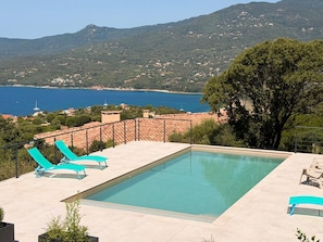 Ein rechteckiger Swimmingpool mit klarem, blauen Rand, umgeben von einer gefliesten Terrasse und zwei blauen Liegestühlen.