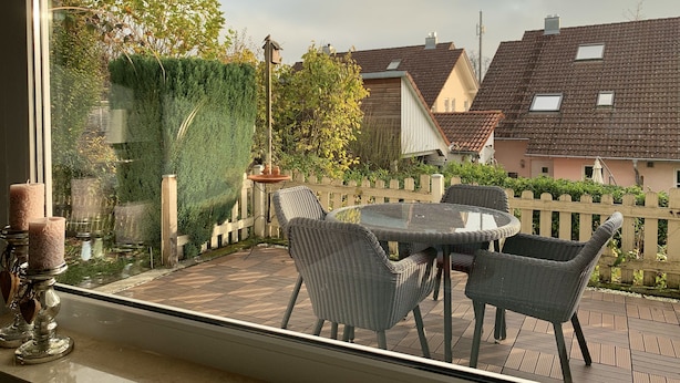 Ein Balkon mit Korbstühlen, einem Tisch, einer Topfpflanze und Blick auf benachbarte Häuser.