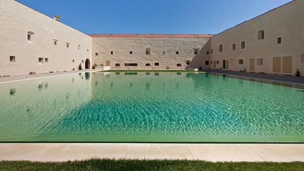 A swimming pool with a clear blue water surface, surrounded by a building with multiple windows and a flat roof.