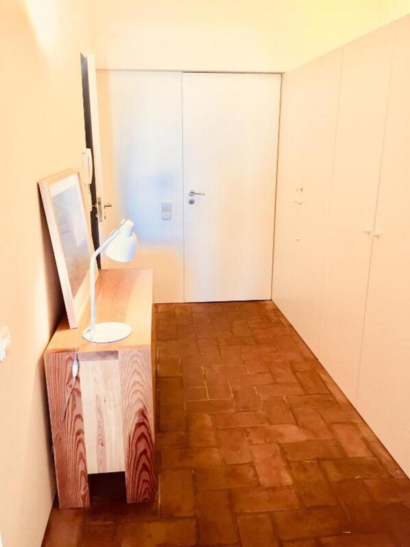 Una stanza piccola con una scrivania in legno, una lampada bianca e una porta chiusa.