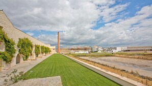 A pathway lined with arches, leading to a building with a tall chimney.