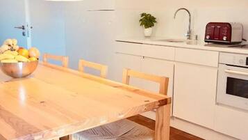 A wooden dining table with chairs, a bowl of fruit, a potted plant, a toaster, and a sink in a kitchen area.