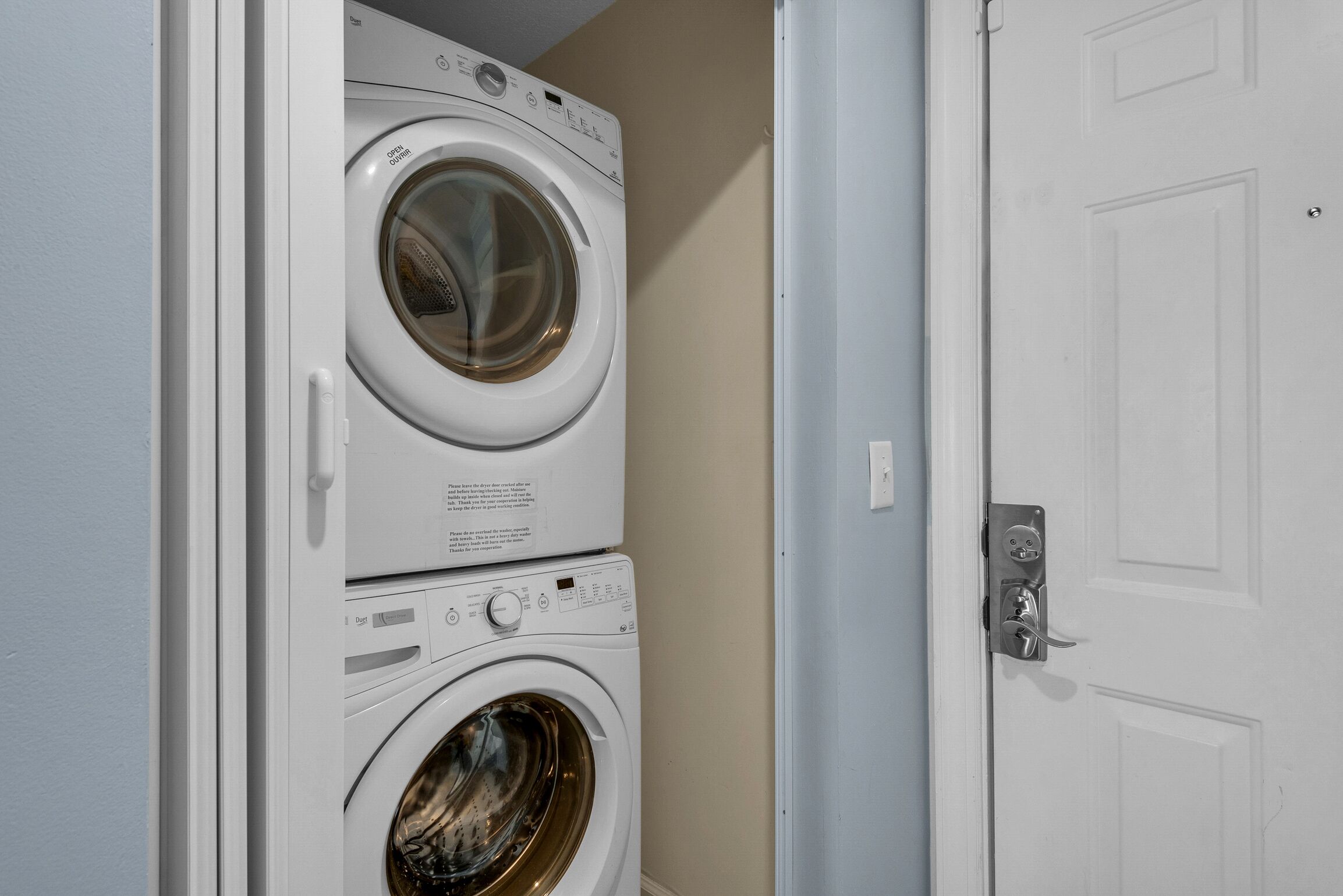 A stacked washer and dryer unit in a room with a white door.