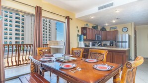 Een eetgedeelte met een houten tafel voor vier personen, een keuken met moderne apparatuur en een balkon met uitzicht op een hoog gebouw.